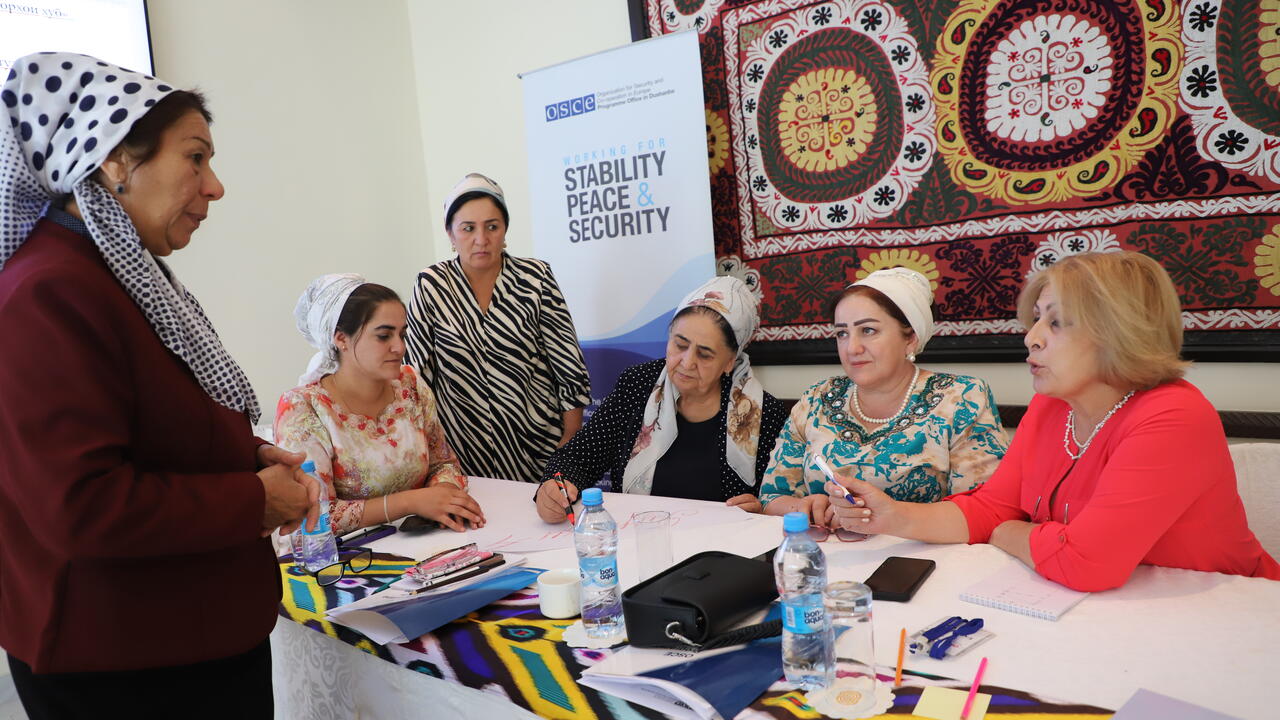 Women in headscarves and business attire sit around a conference table, engaged in discussion.